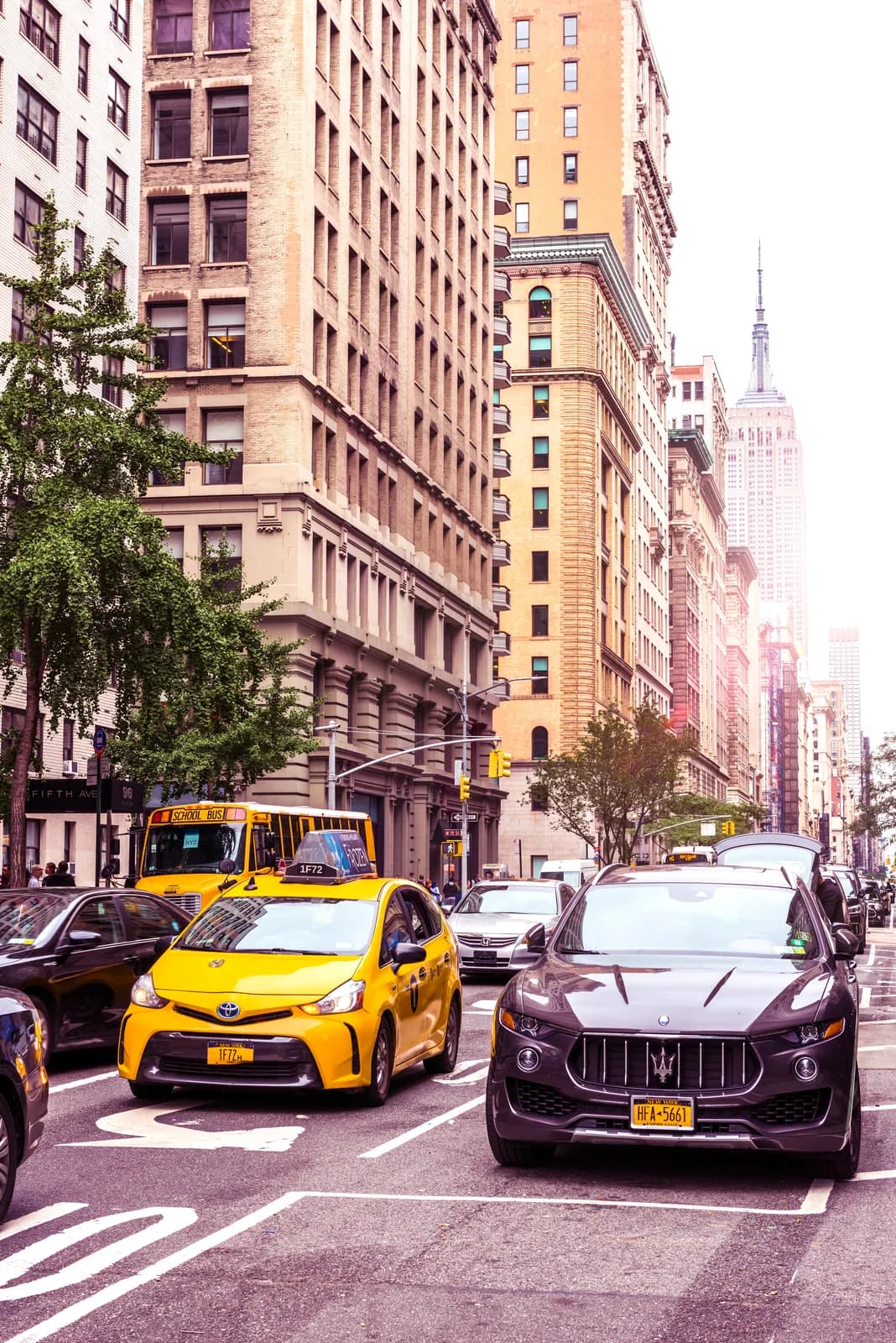 Fifth Avenue traffic between prewar stone buildings, with the Empire State Building in the haze beyond