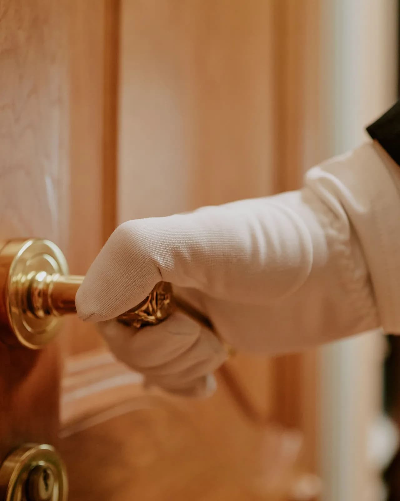 A white-gloved hand turning the brass handle of a polished wood door
