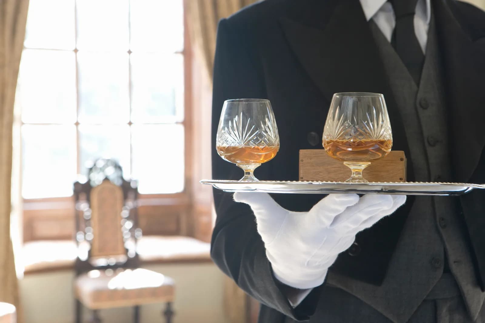 A tray of two cut-crystal glasses of whisky carried in a white-gloved hand