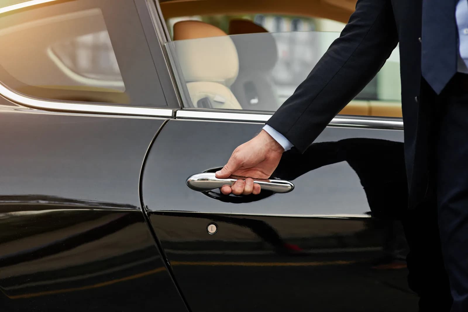 A hand in a dark suit sleeve on the chrome handle of a black car door