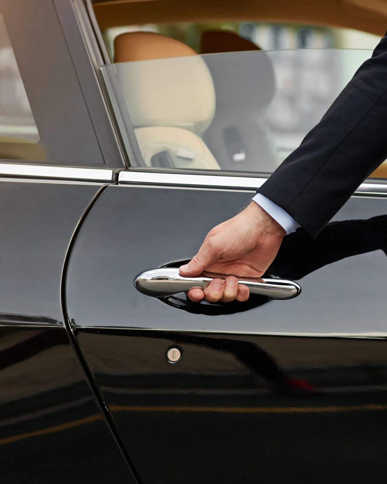 A hand in a dark suit sleeve on the chrome handle of a black car door