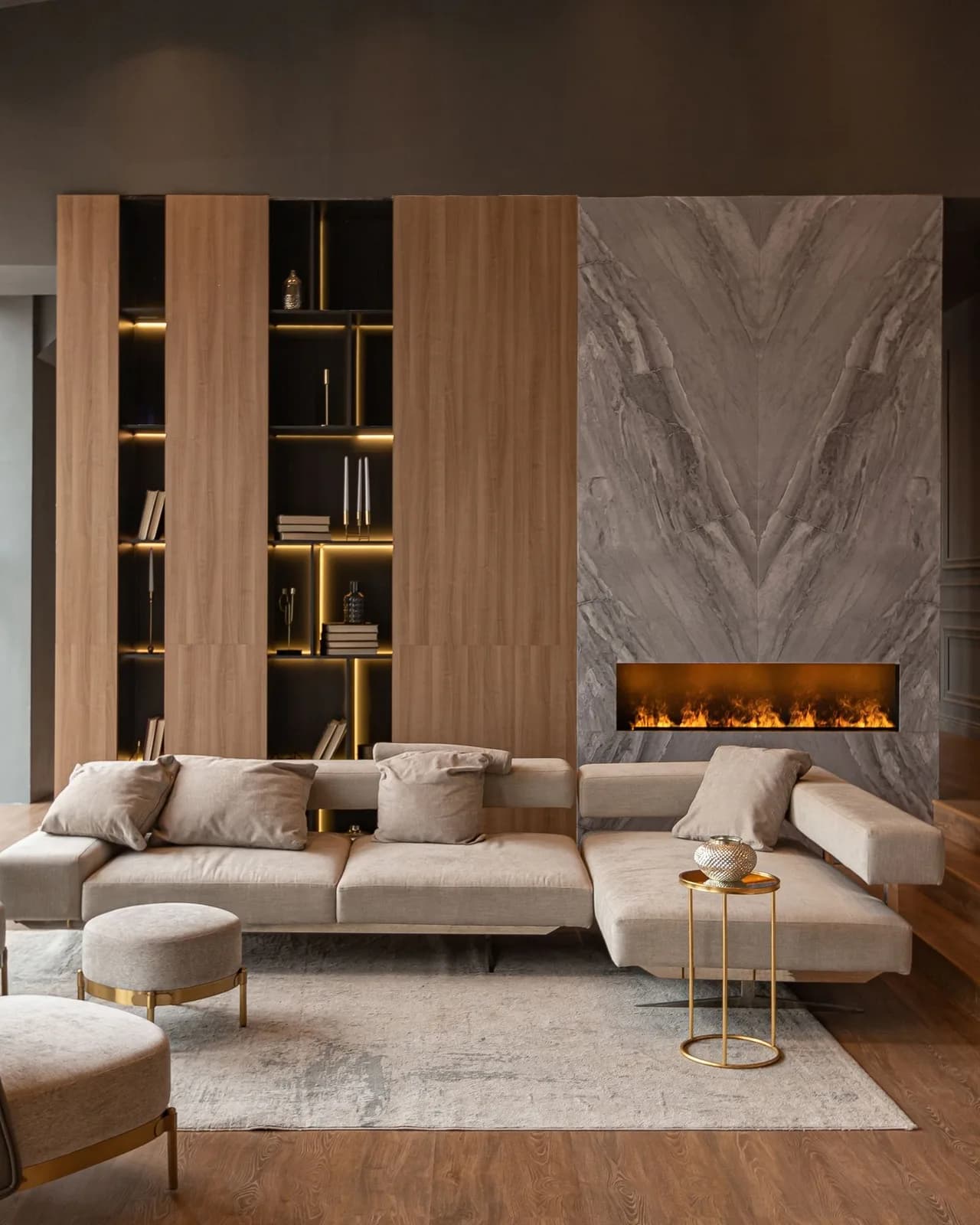 A living room with a lit marble fireplace, a low sectional sofa and a wood panelled bookcase wall