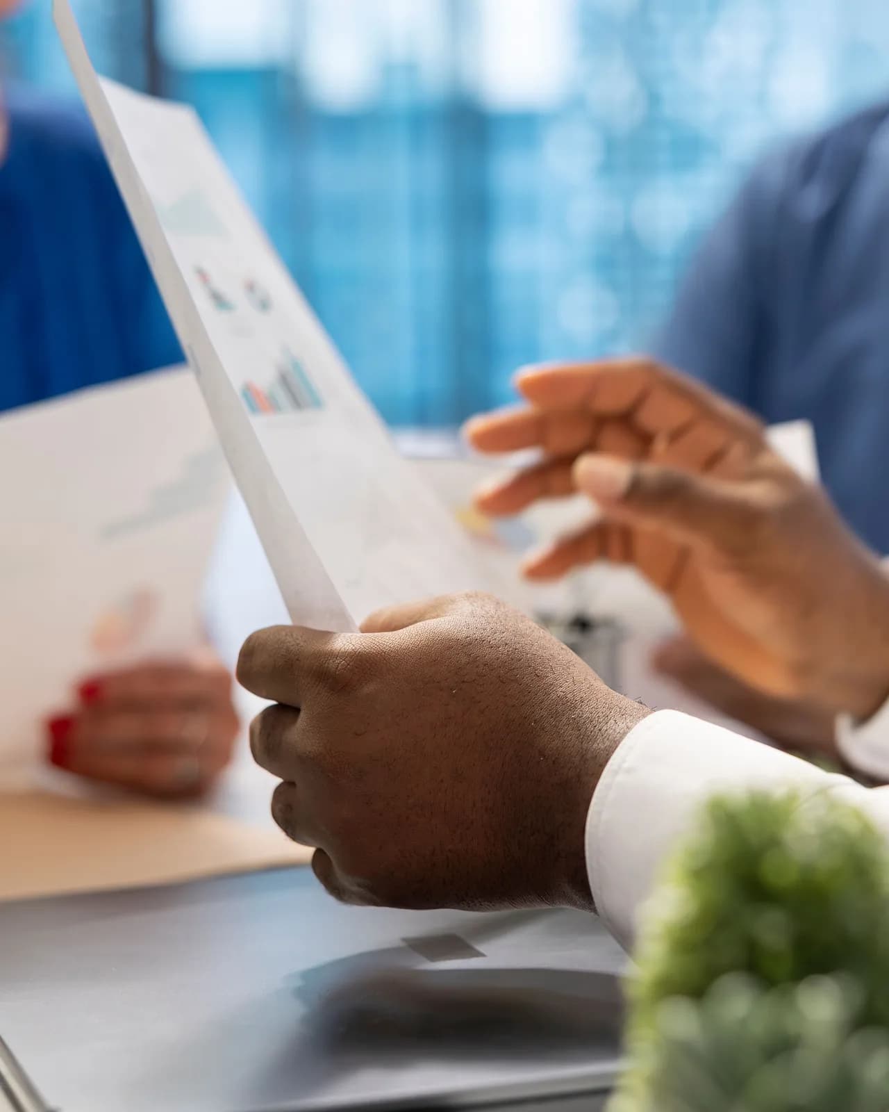 Hands holding a printed bar chart across a table, with two people either side