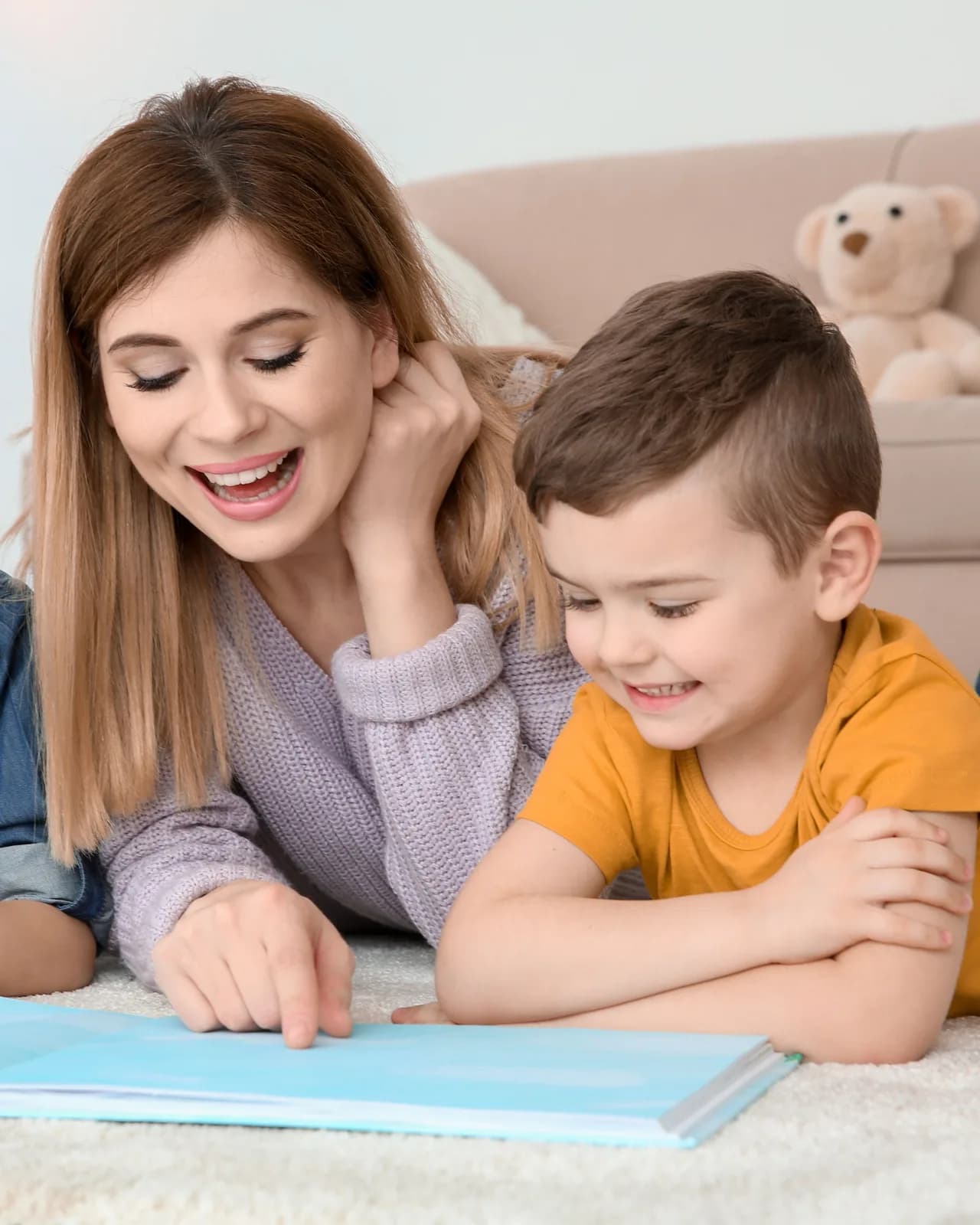 A woman and a young boy lying on a rug, reading an open picture book together