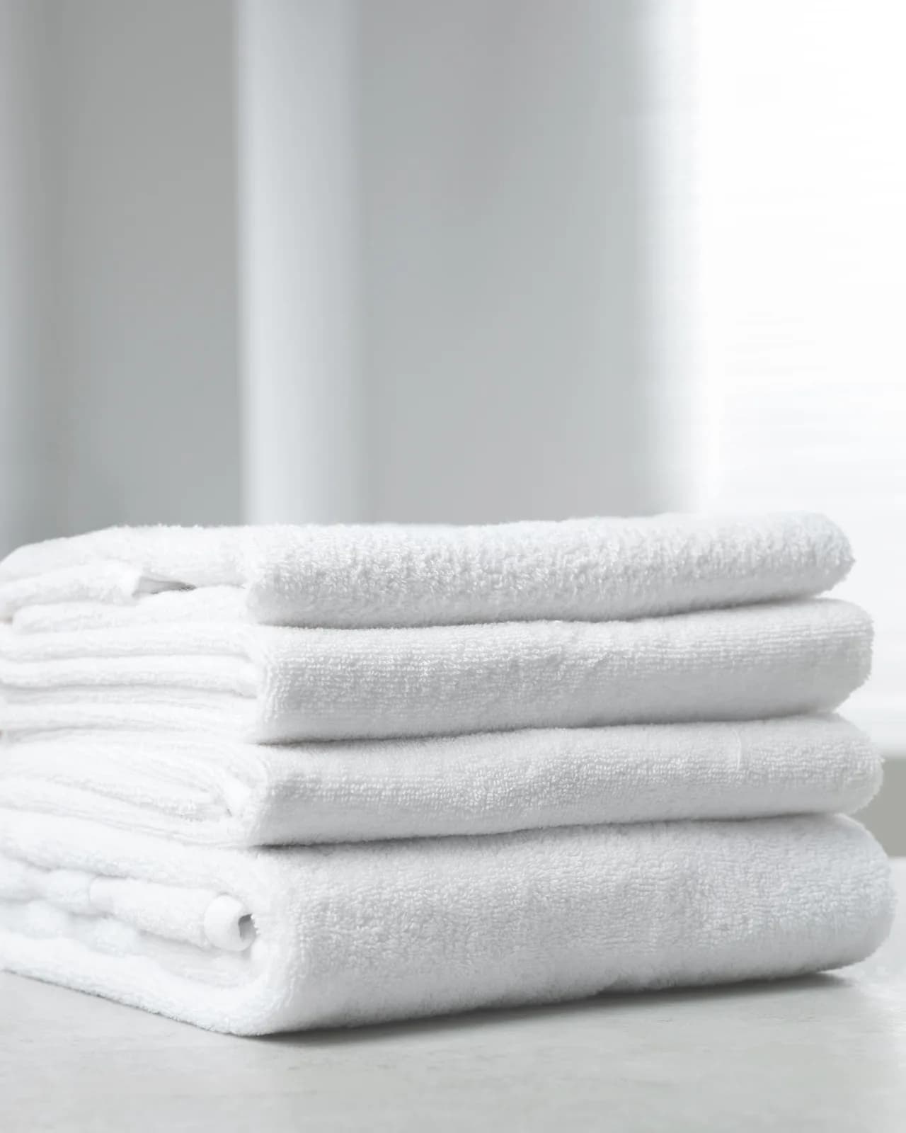 Folded white bath towels stacked on a stone counter in a bright bathroom