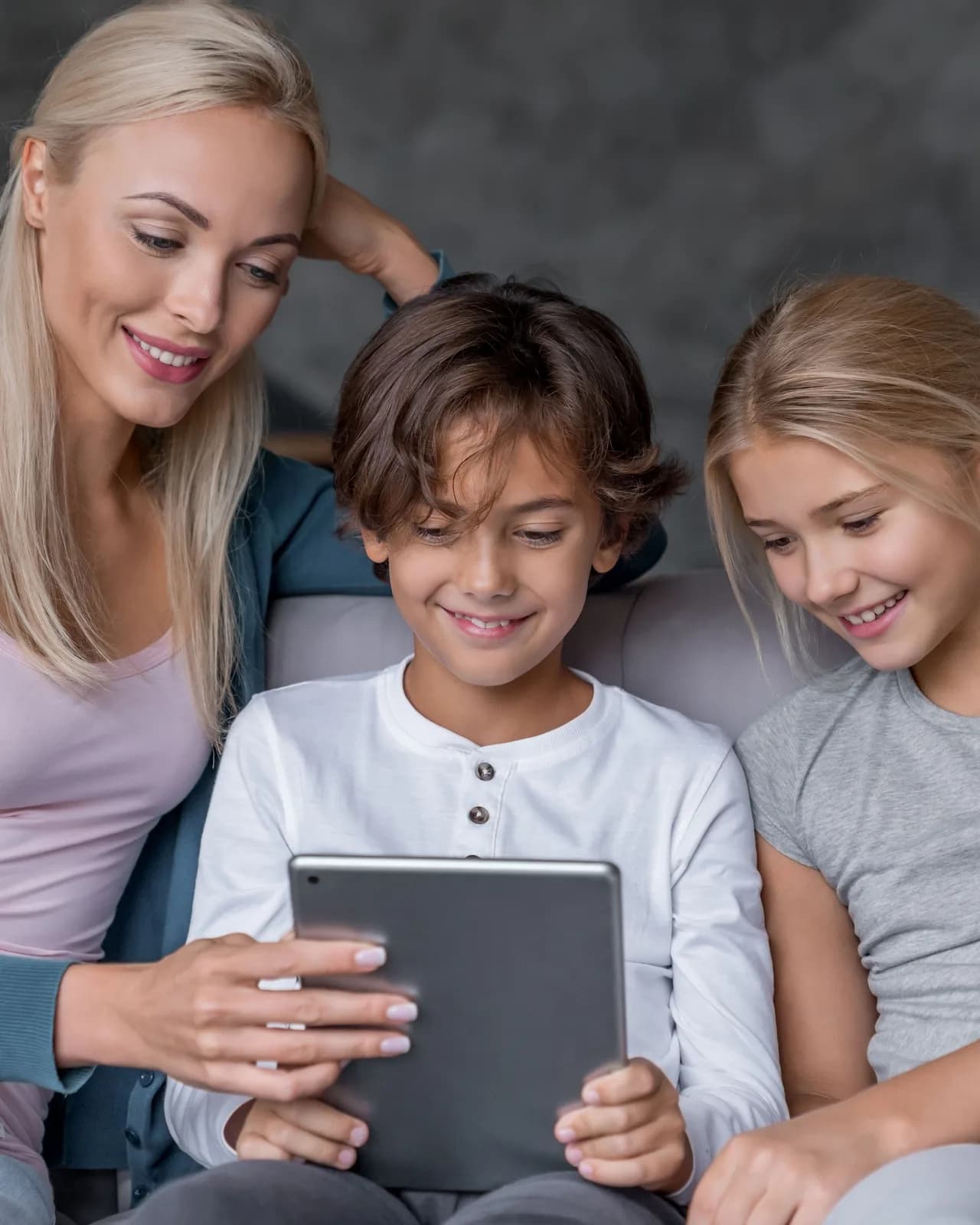 A woman and two children looking at a tablet together on a sofa