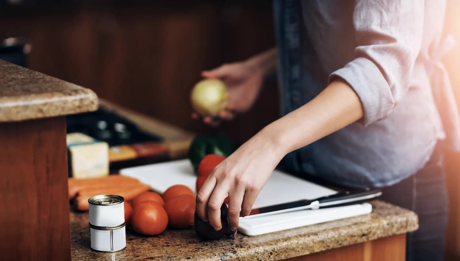 A cook's hands at a stone counter with an onion, tomatoes and a chopping board