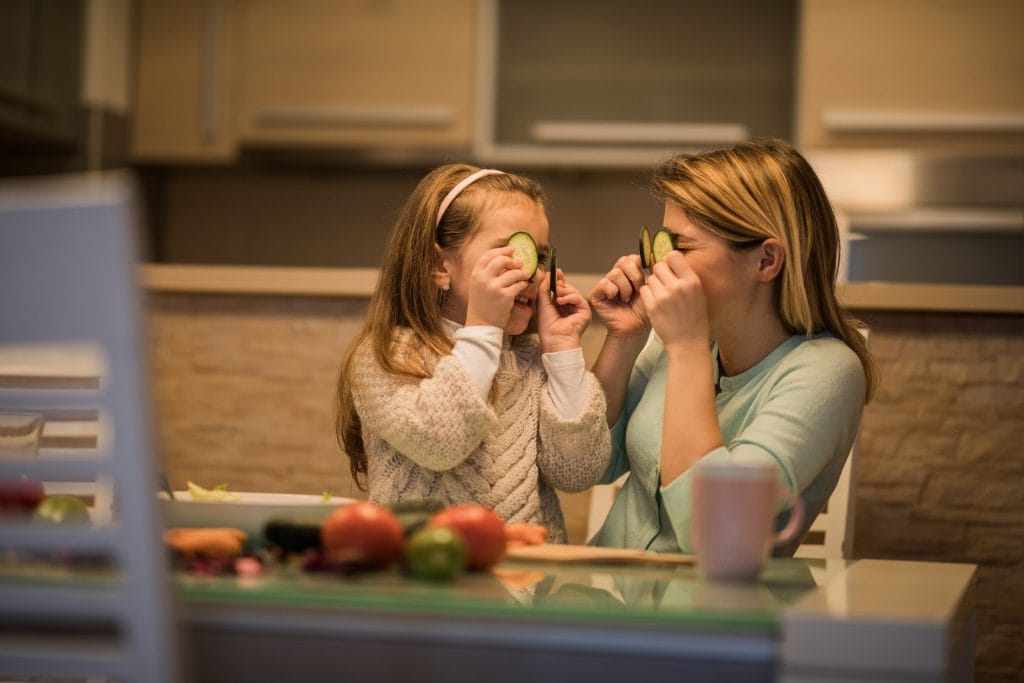 Playful mother and daughter covering their eyes with slices of cucumber. domestic staff hire